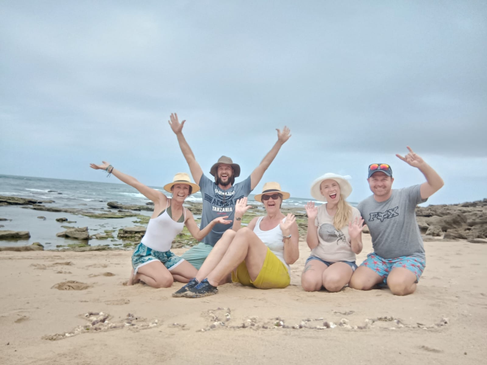 Five friends kneeling on a rocky beach with their arms raised