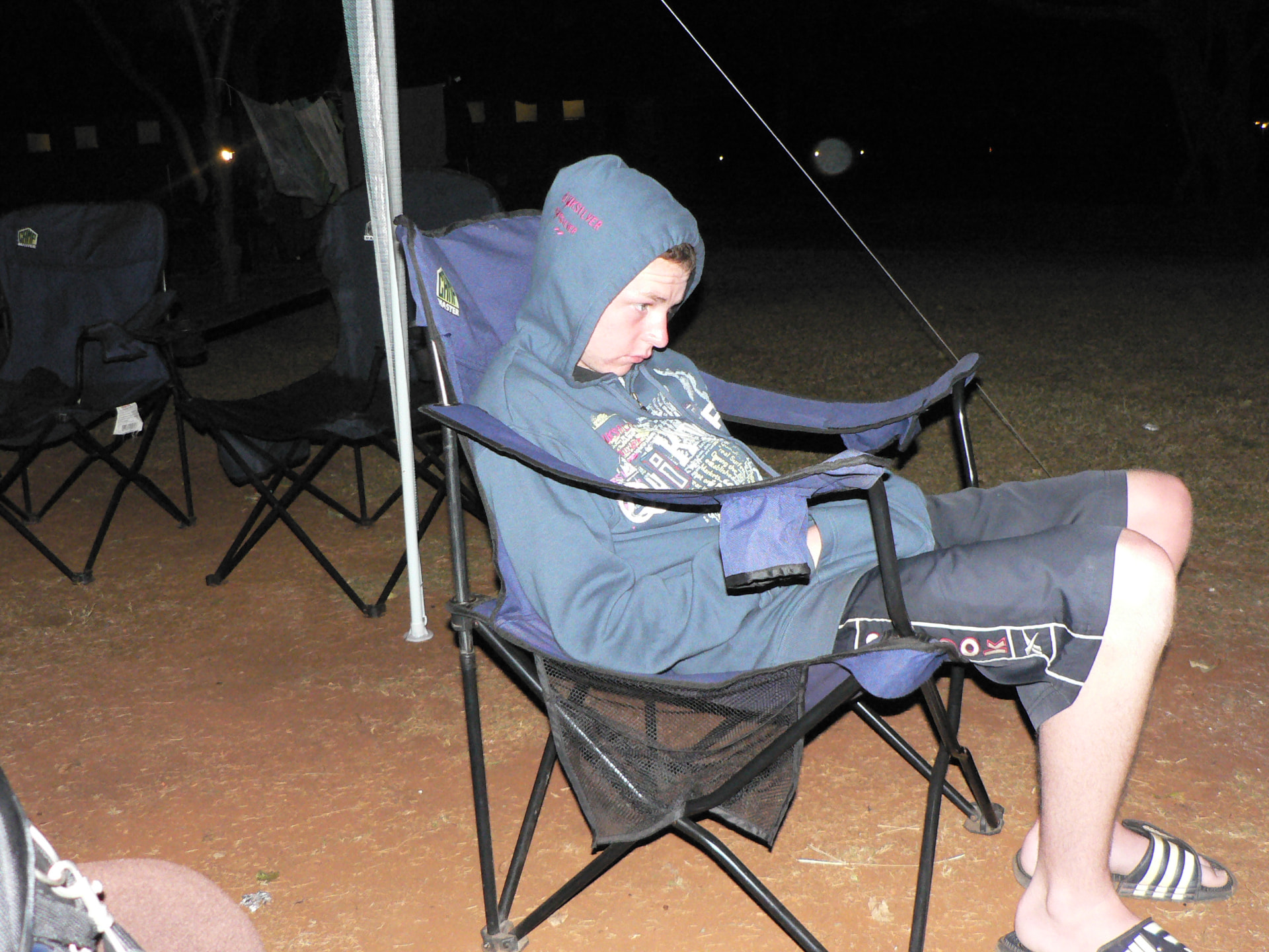 A young Angelo sitting in a camping chair at night, wearing a blue hoodie