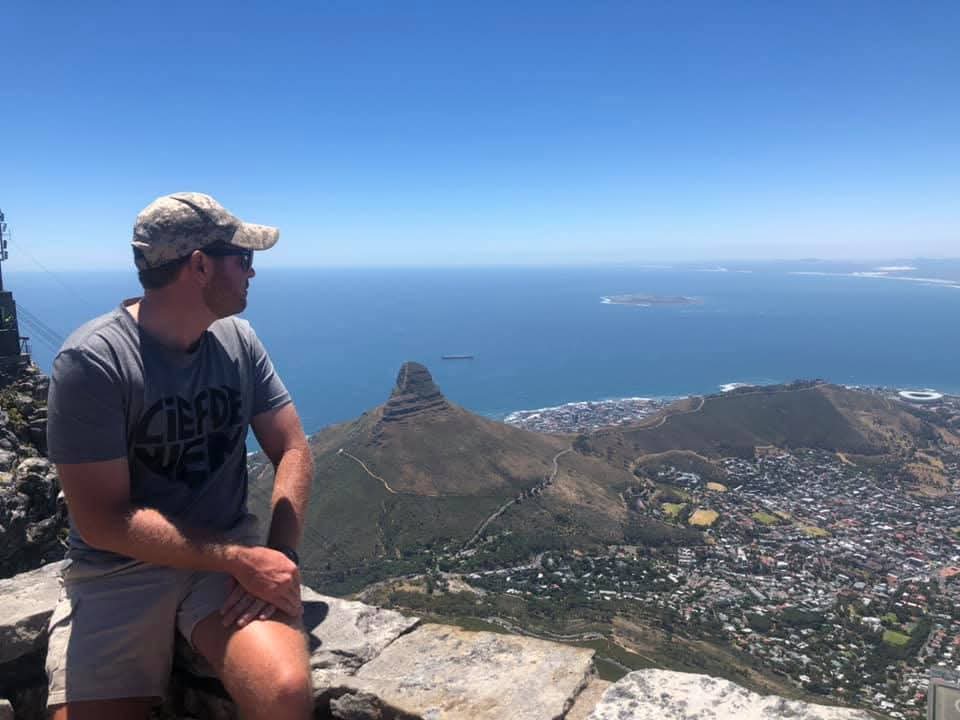 Angelo sitting on a mountain ledge overlooking the city and ocean coastline
