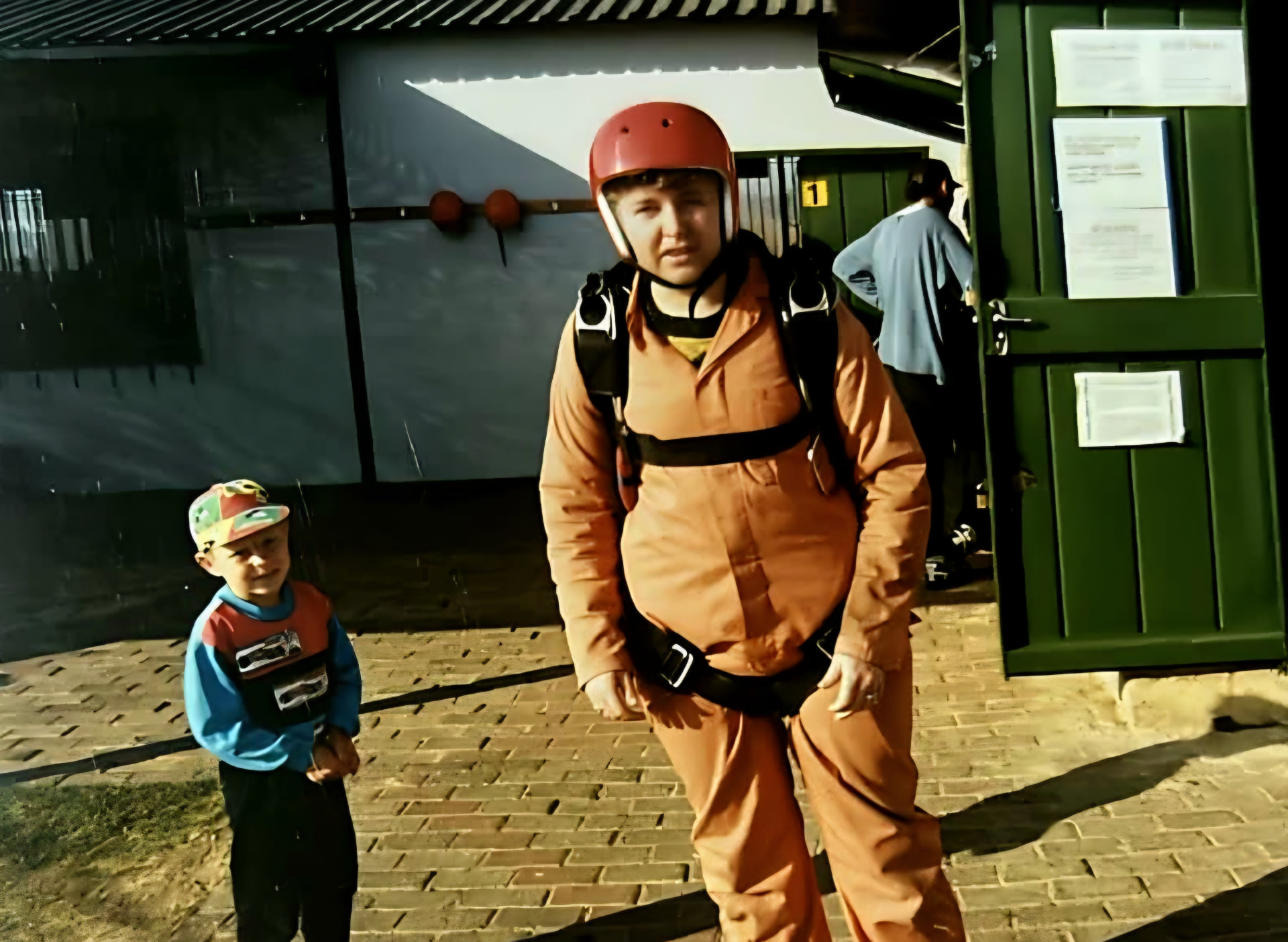 A small boy in a cap beside a man in an orange jumpsuit and helmet