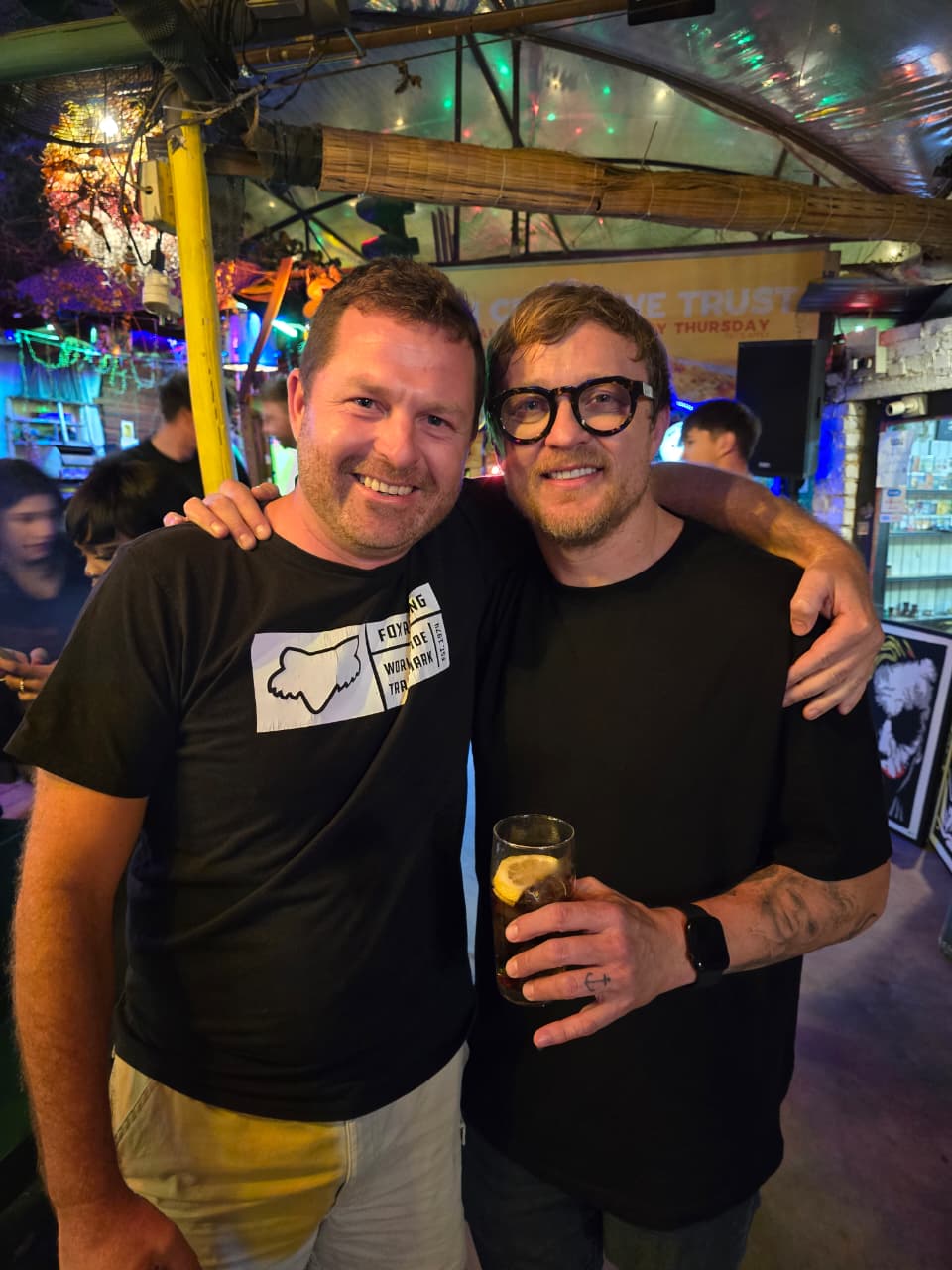 Angelo and Francois van Coke arm in arm at a bar, one holding a drink