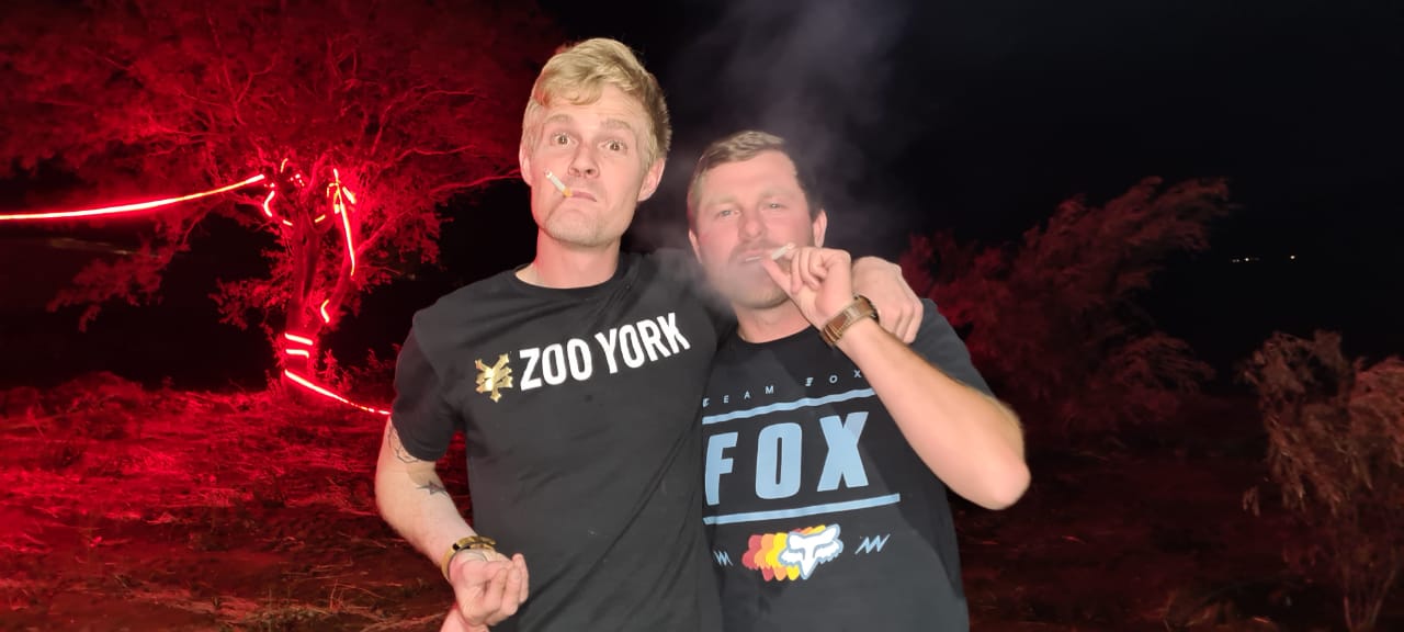 Angelo and a friend posing at night under red lights in the bush