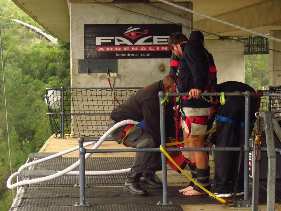 Angelo smiling beside his smiling instructor while another is harnessed up on the Face Adrenalin platform