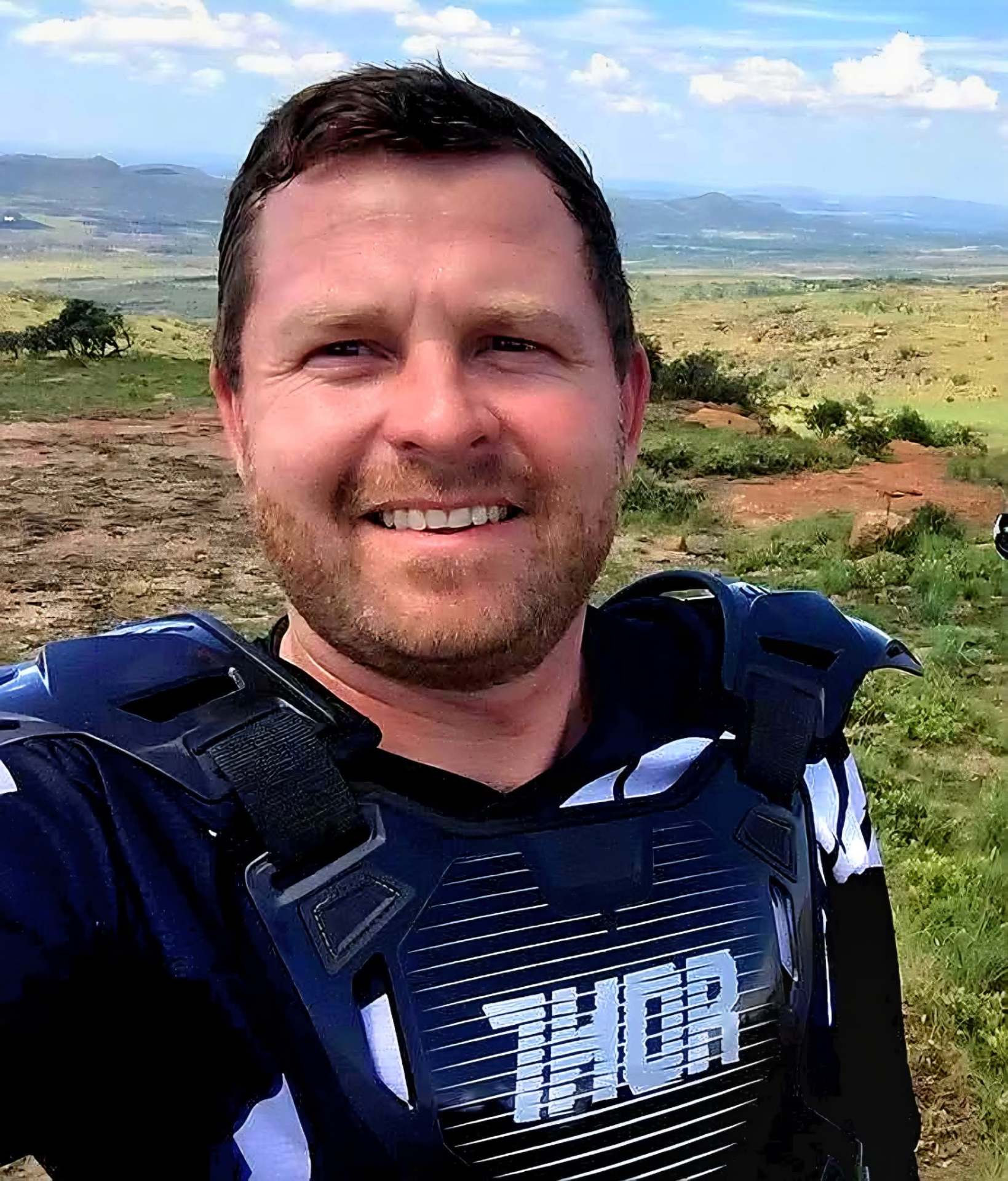 Angelo smiling in motocross chest armour with hills and open plains behind him