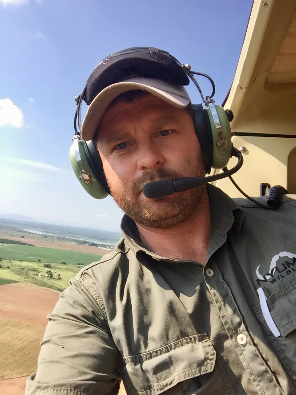 Angelo wearing an aviation headset in a helicopter, green fields below