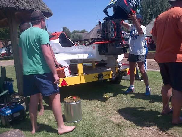 Angelo and friends lifting a boat motor onto a trailer on the grass