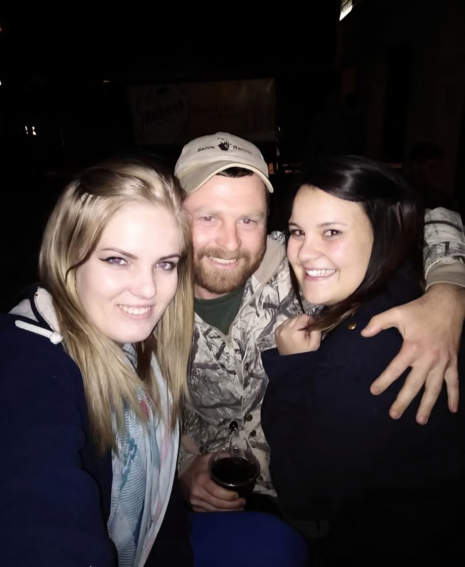 A friend standing between two smiling women at night