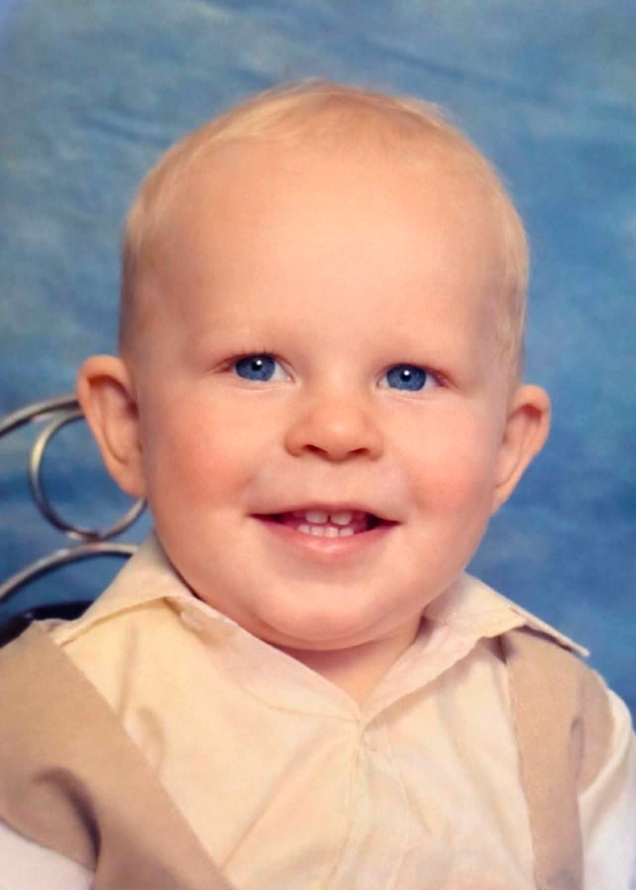 A baby portrait of Angelo as a smiling toddler with blond hair and blue eyes