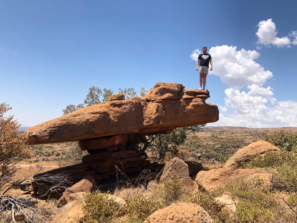 Angelo standing on top of a balancing mushroom-shaped rock in dry bushveld