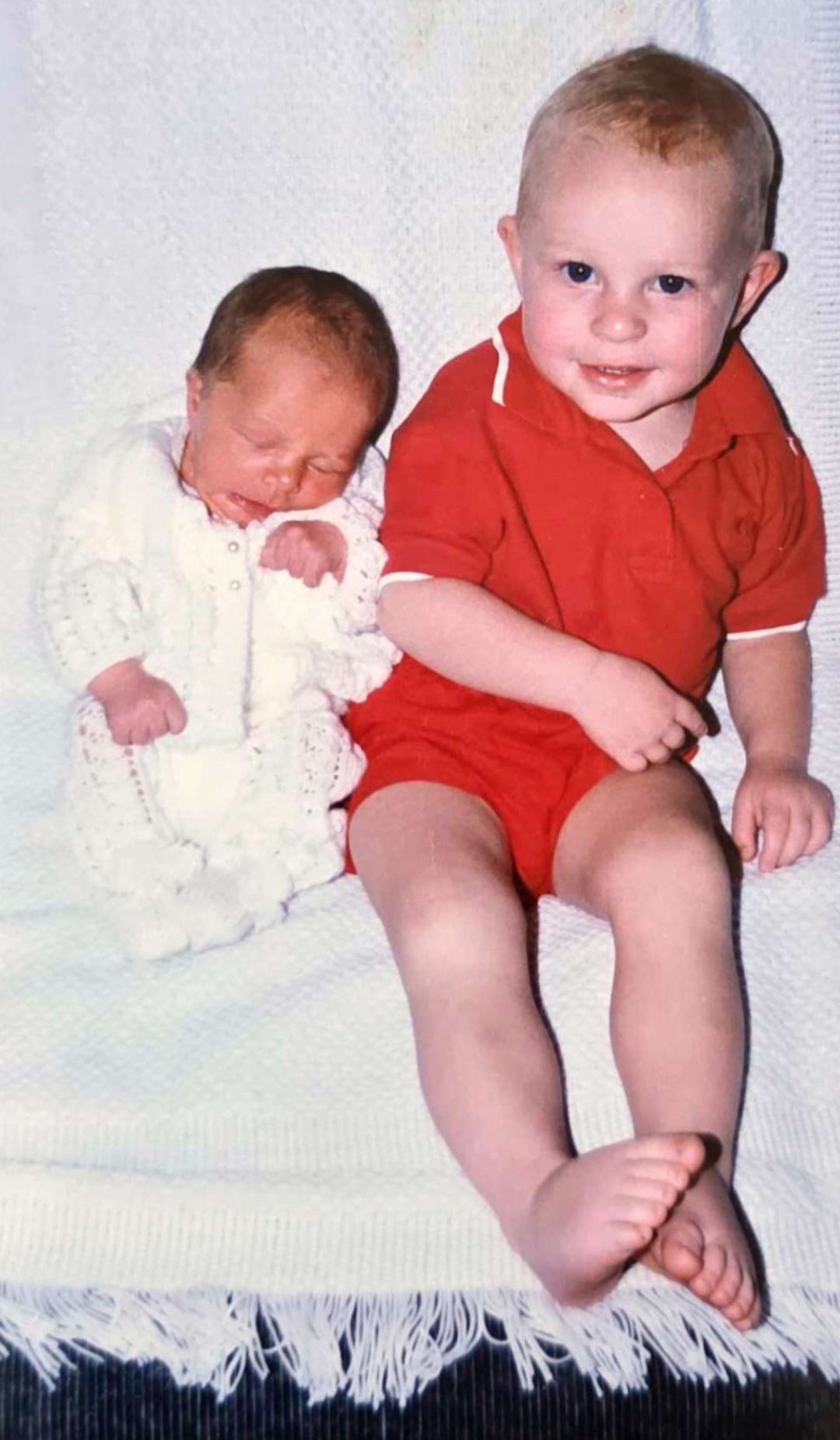Angelo as a little boy in red sitting beside his newborn sibling