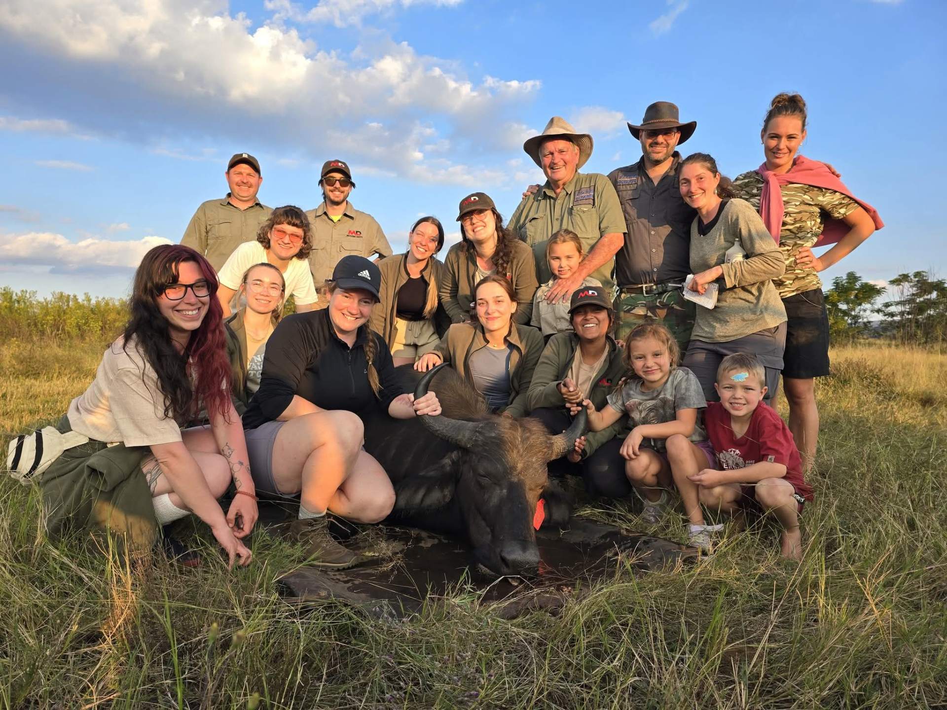 Students Angelo worked with and a group gathered beside a buffalo in warm afternoon light