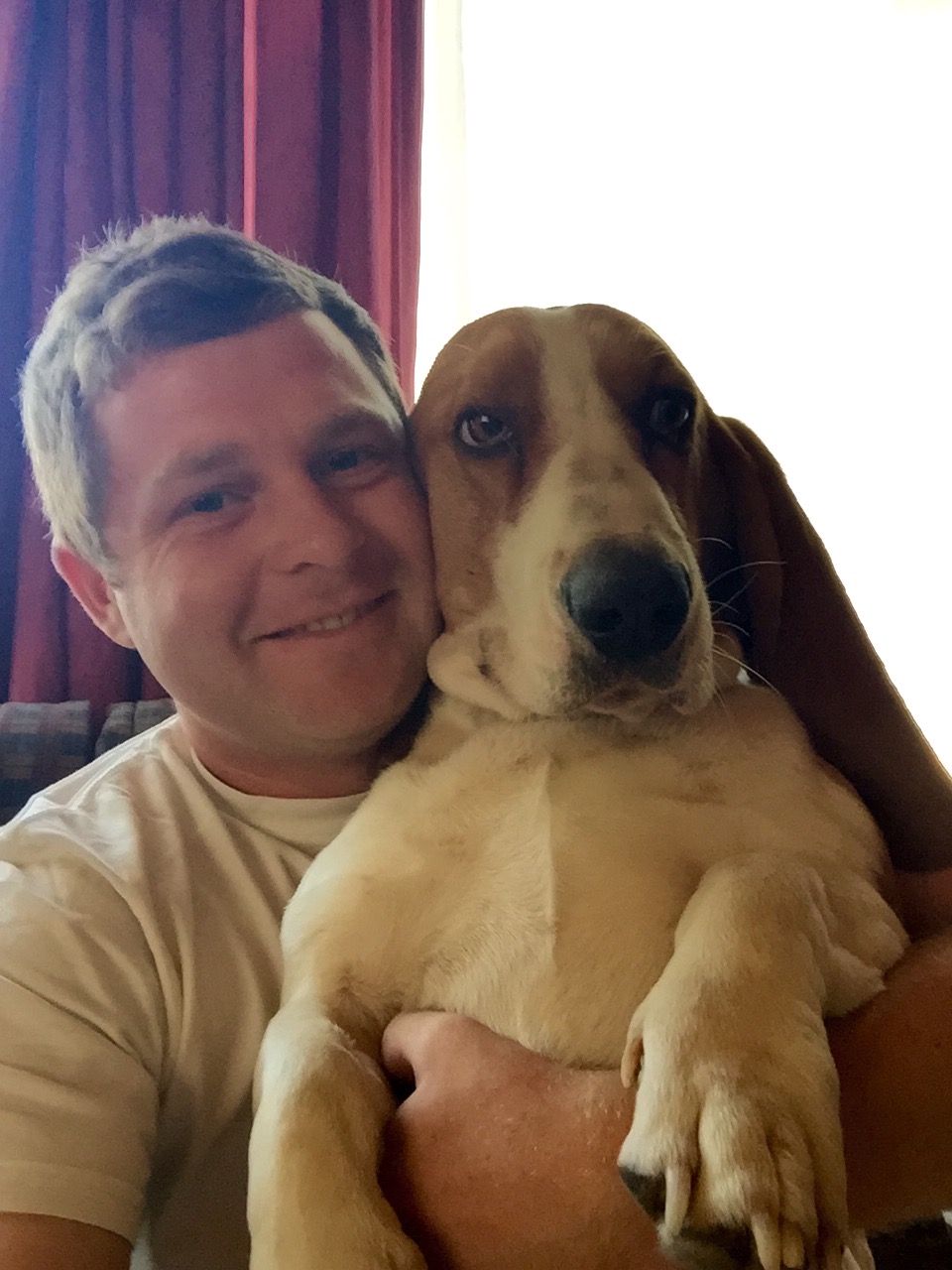 Angelo smiling on the couch while holding a basset hound