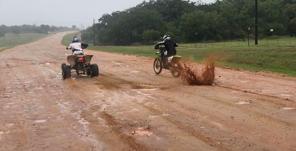 A companion on a dirt bike throwing up a big splash of mud beside Angelo on his quad