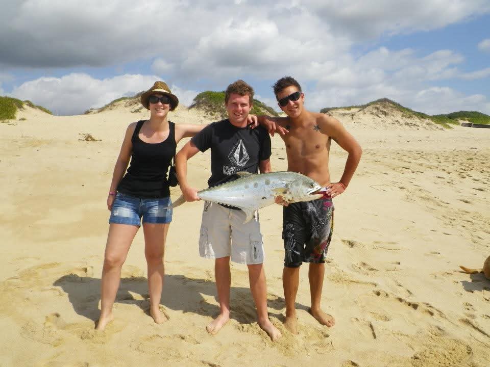 Three friends on the dunes holding a large kingfish together