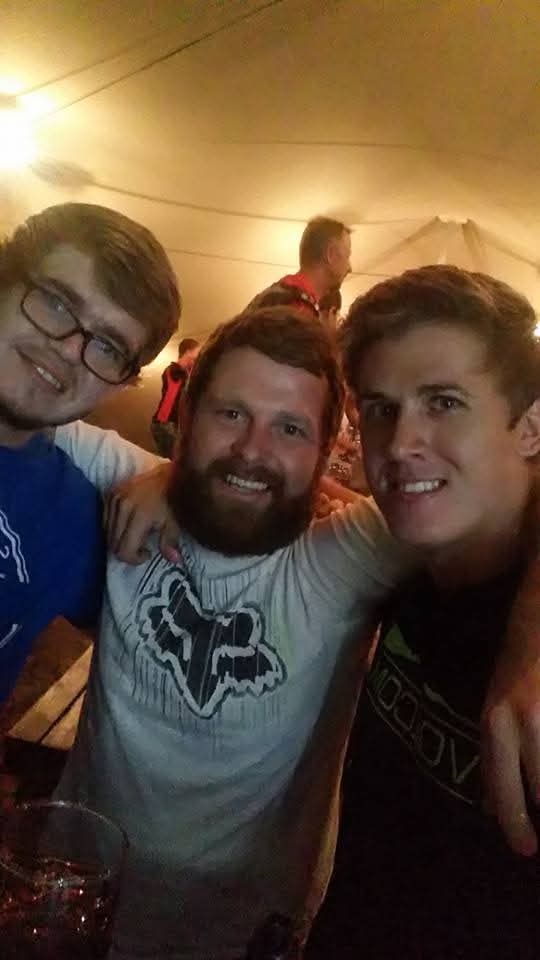 Three friends with arms around each other inside a lit marquee tent