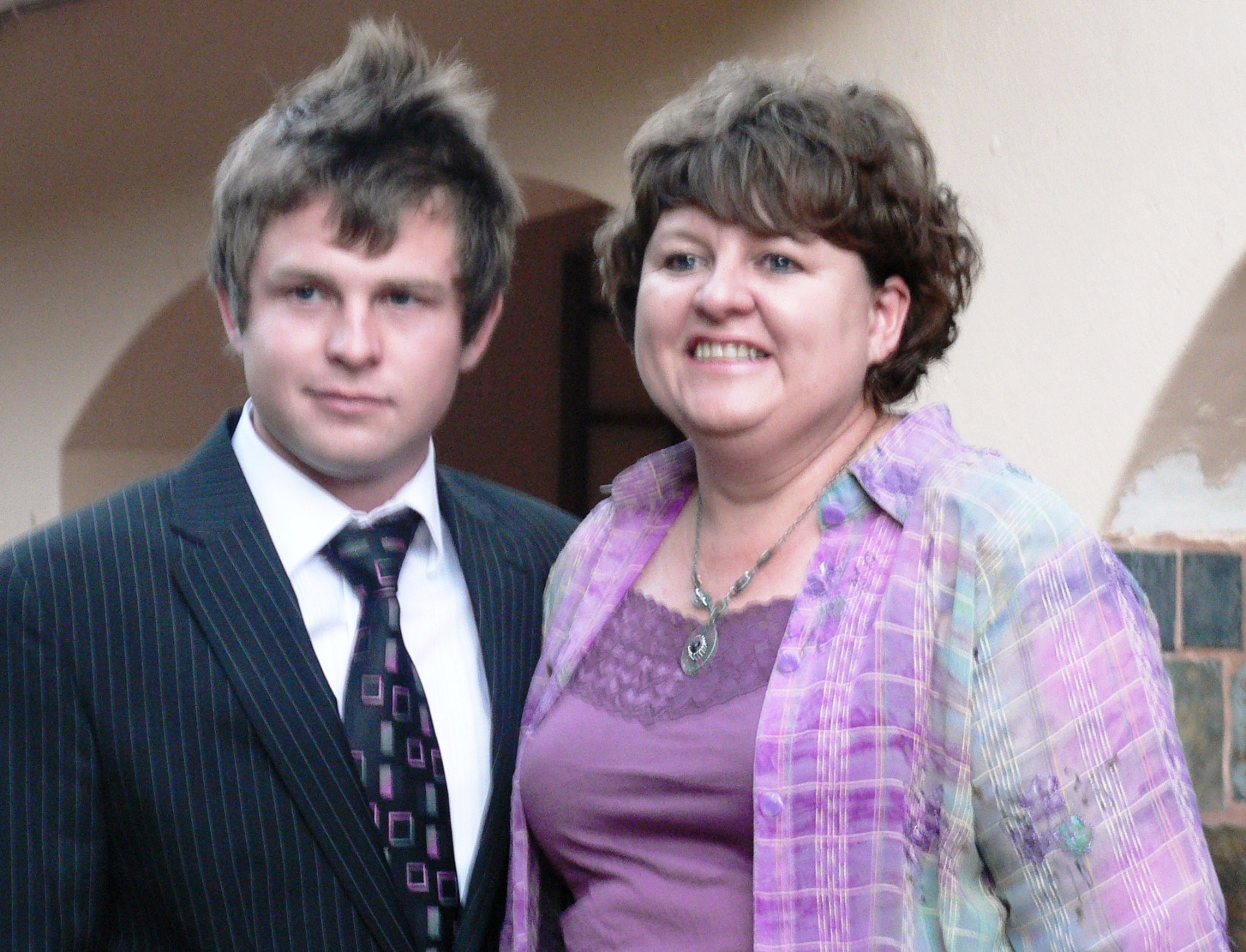 Angelo in a suit smiling beside a family member in purple