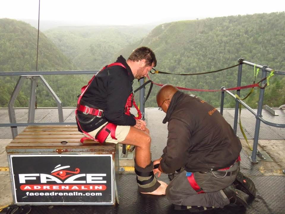 Angelo seated on the Face Adrenalin platform while an instructor secures the bungy straps around his ankles