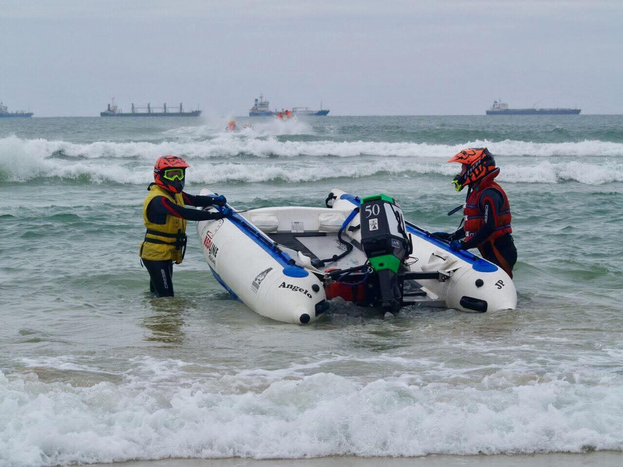 Angelo and a teammate launching their racing boat through the shore break