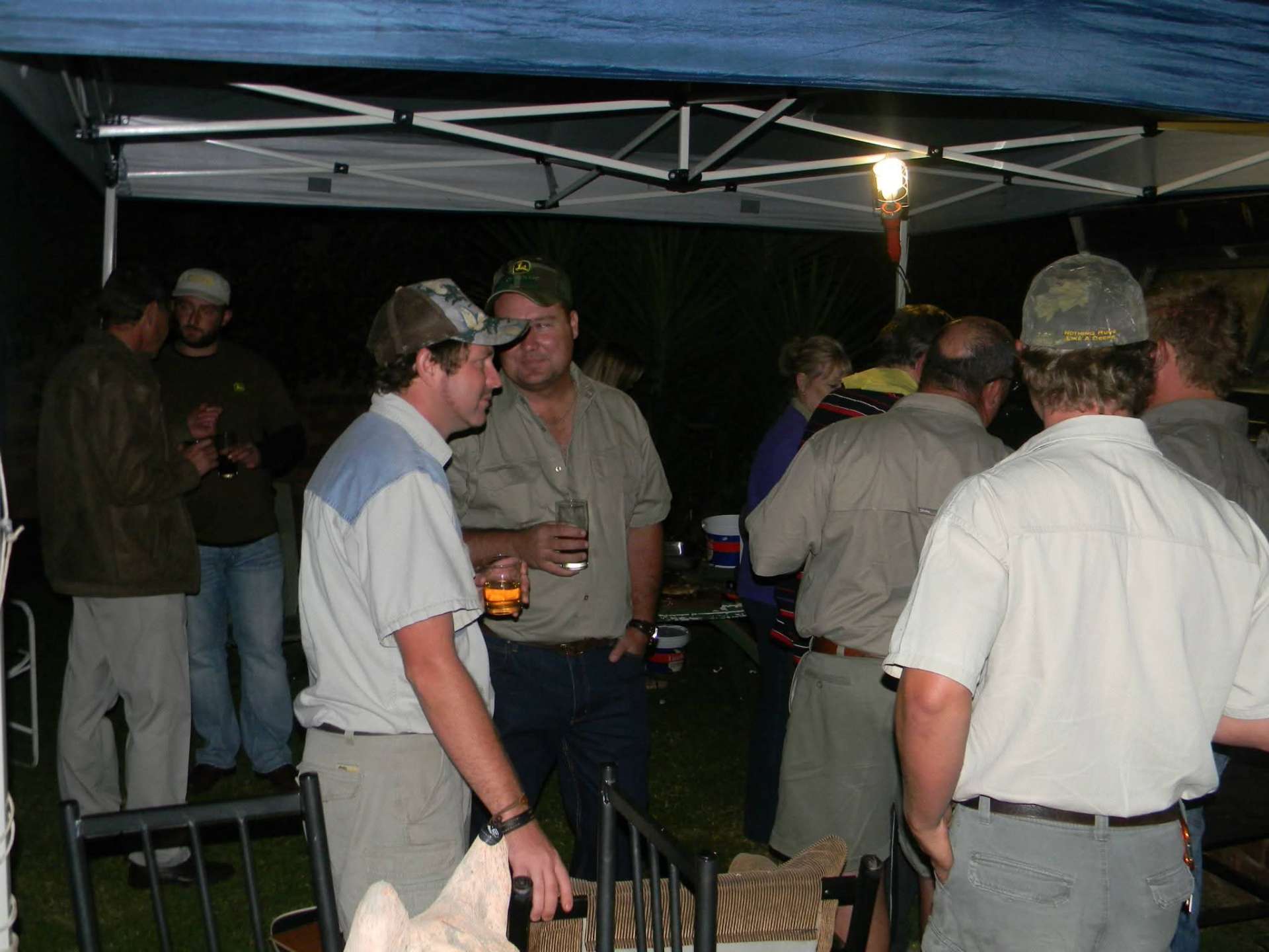 Angelo and friends sharing drinks under a lit gazebo at a braai