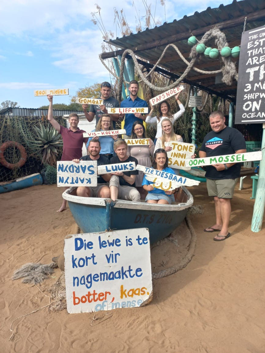 A group of friends holding Afrikaans signs around an old blue boat