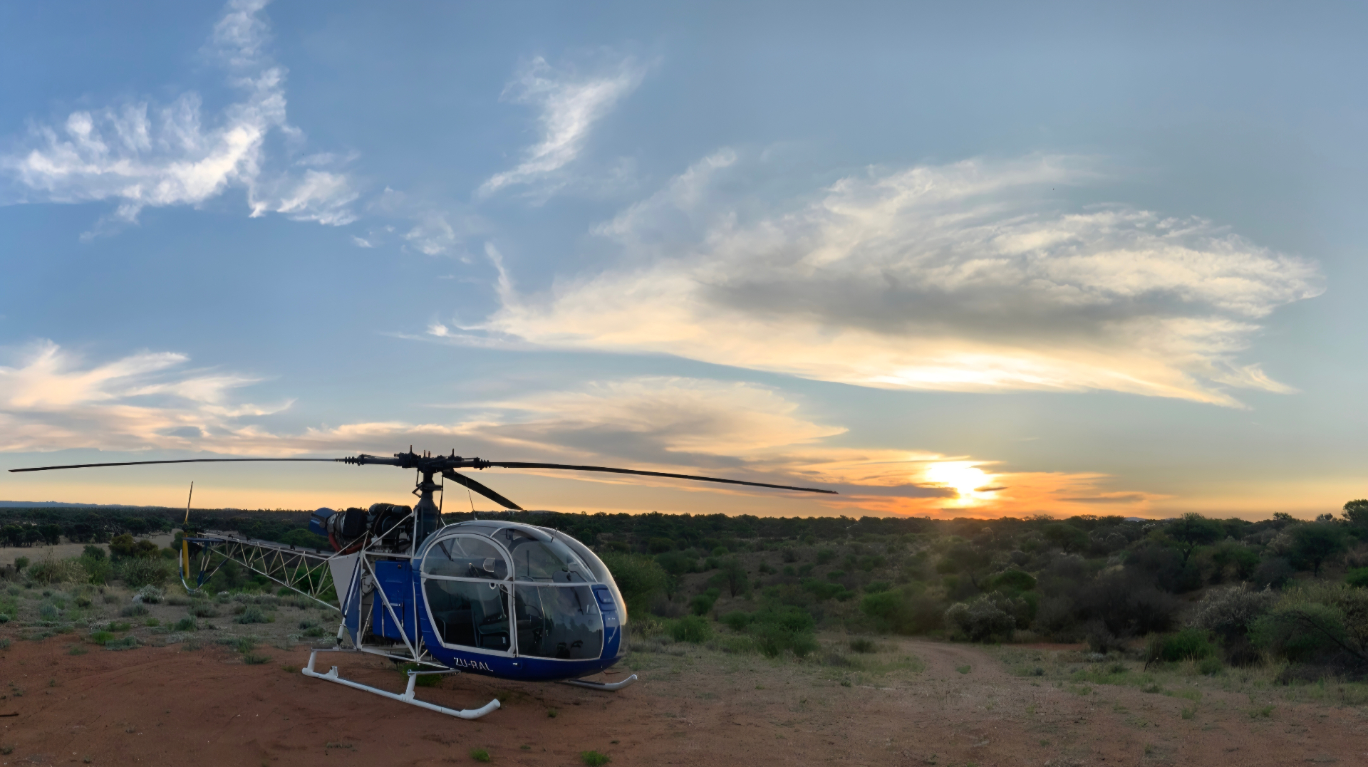A helicopter standing on a bush airstrip beneath a wide African sky at sunset