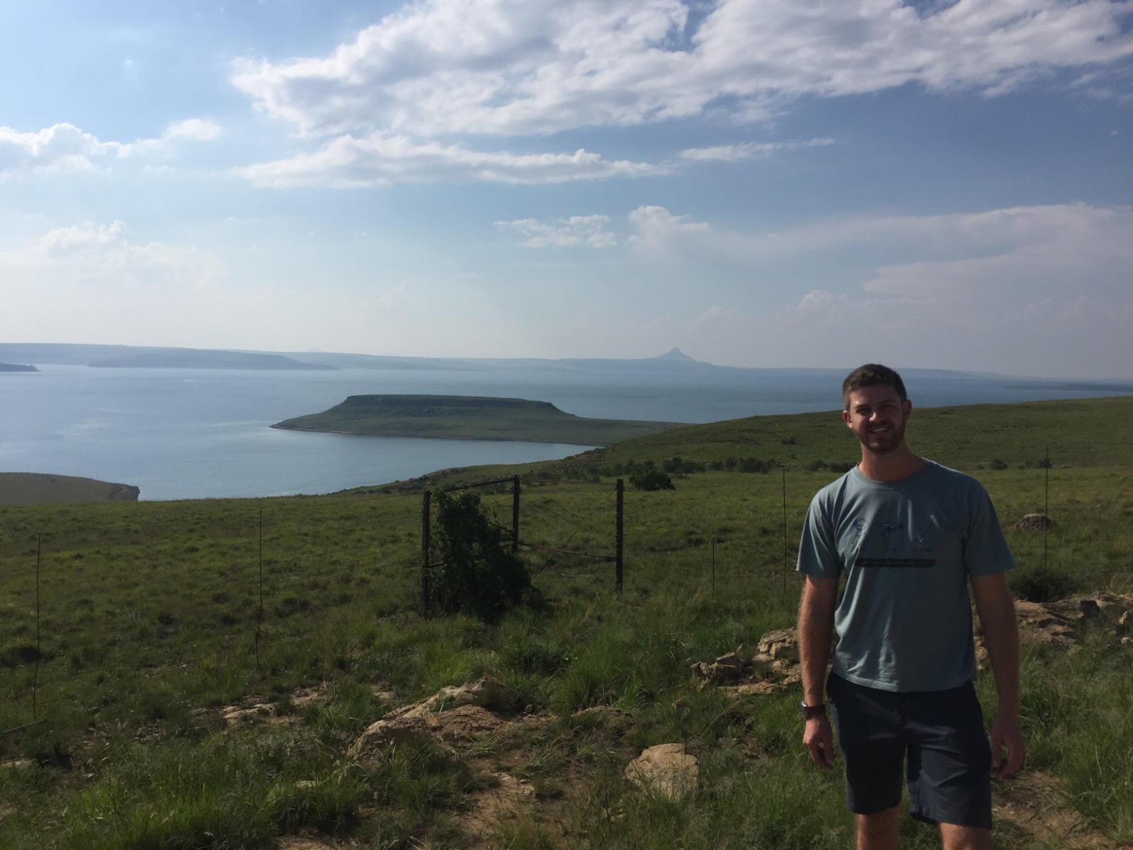 Angelo standing on a grassy overlook above a wide lake with a flat-topped island across the water