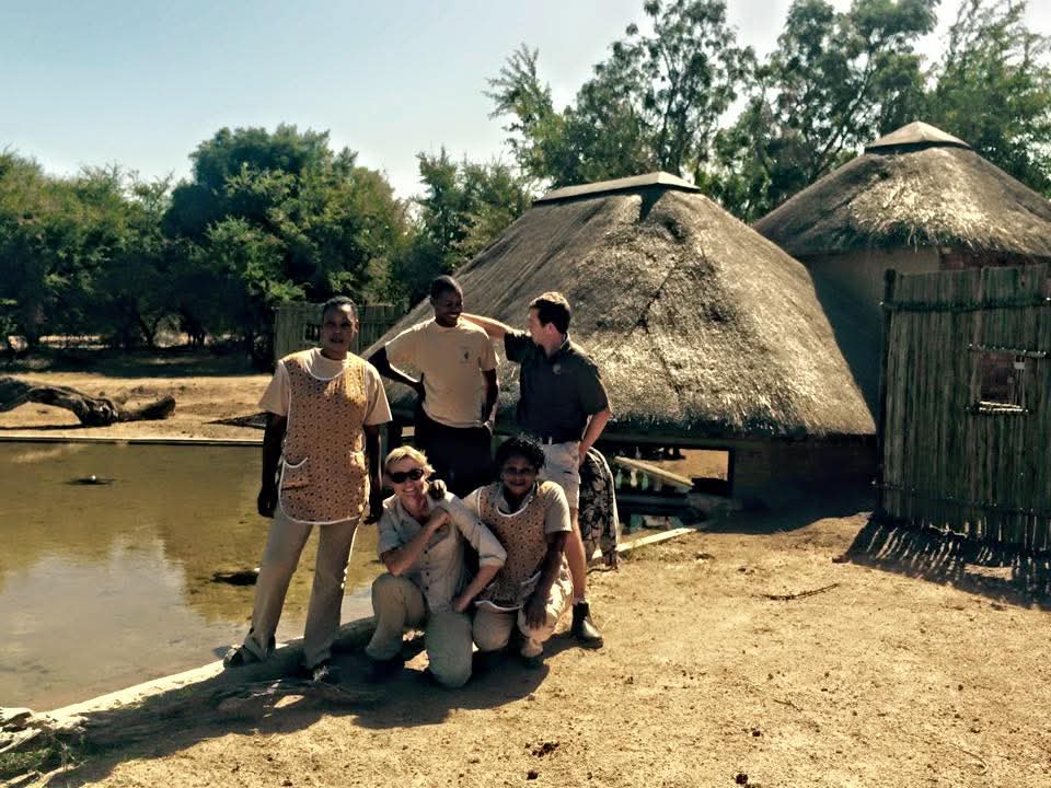 Angelo with a group beside a pond and thatched buildings