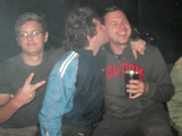 A friend kissing Angelo's cheek while he laughs with a drink at night