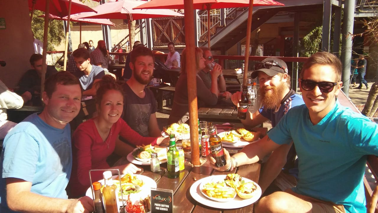 Angelo and friends sharing lunch under red umbrellas at an outdoor restaurant