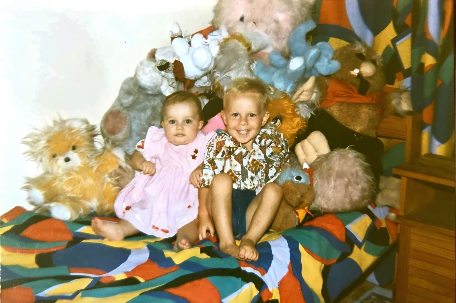 Two little children sitting among a pile of teddy bears