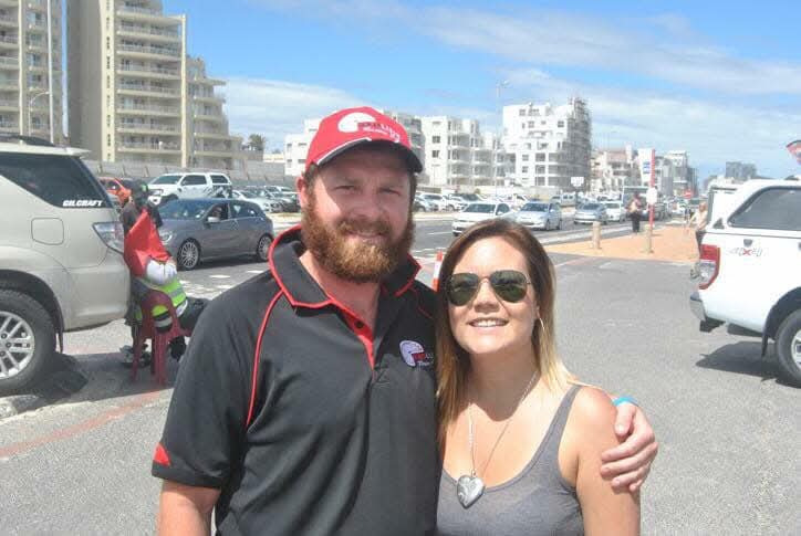 Angelo in a red cap smiling with a woman beside a sunny seaside street