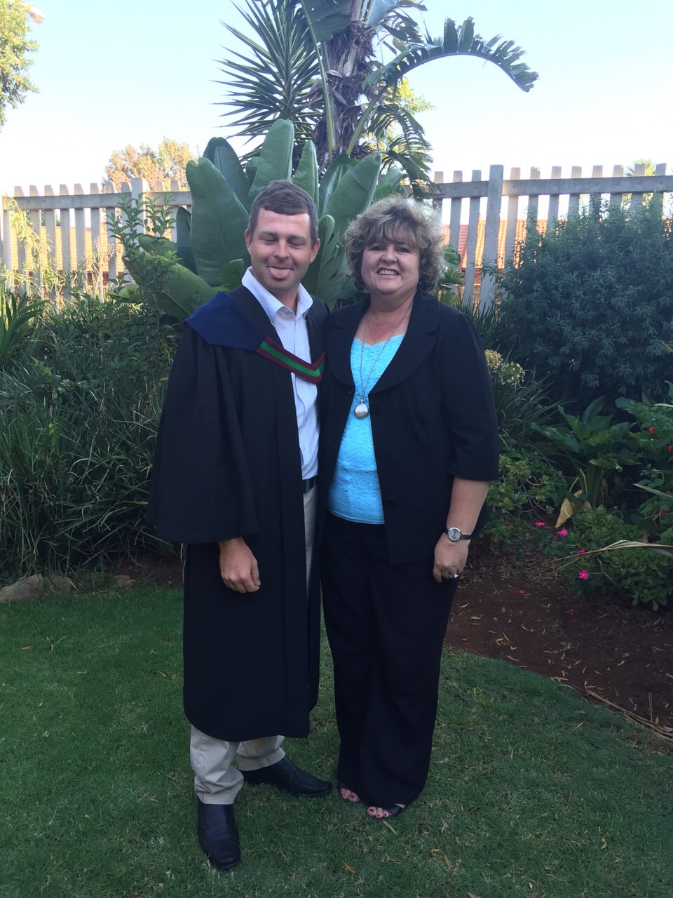 Angelo in his graduation gown standing beside his mother in the garden