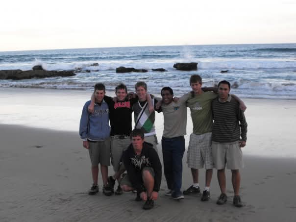 A group of friends standing arm in arm on a beach with waves behind them