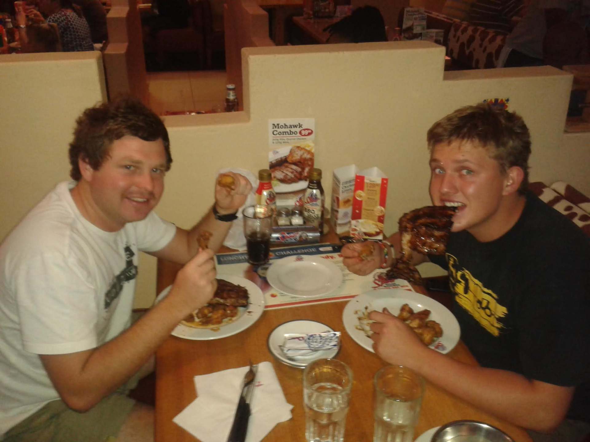 Two young men laughing while eating ribs at a restaurant table