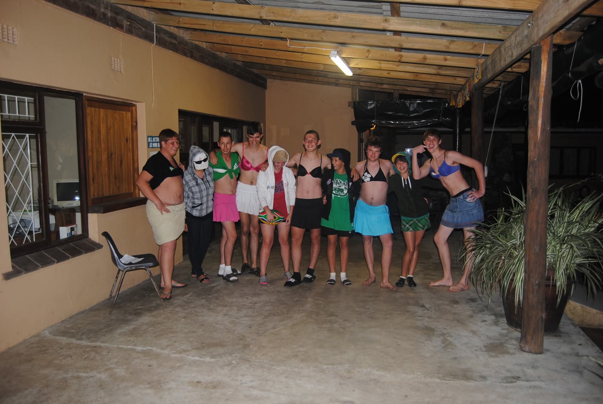 A group of friends in fancy-dress bras and skirts posing under a patio