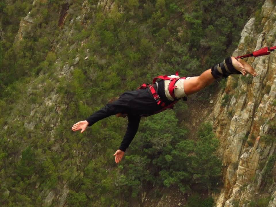 Angelo swinging over the cliff face mid-jump with arms spread wide