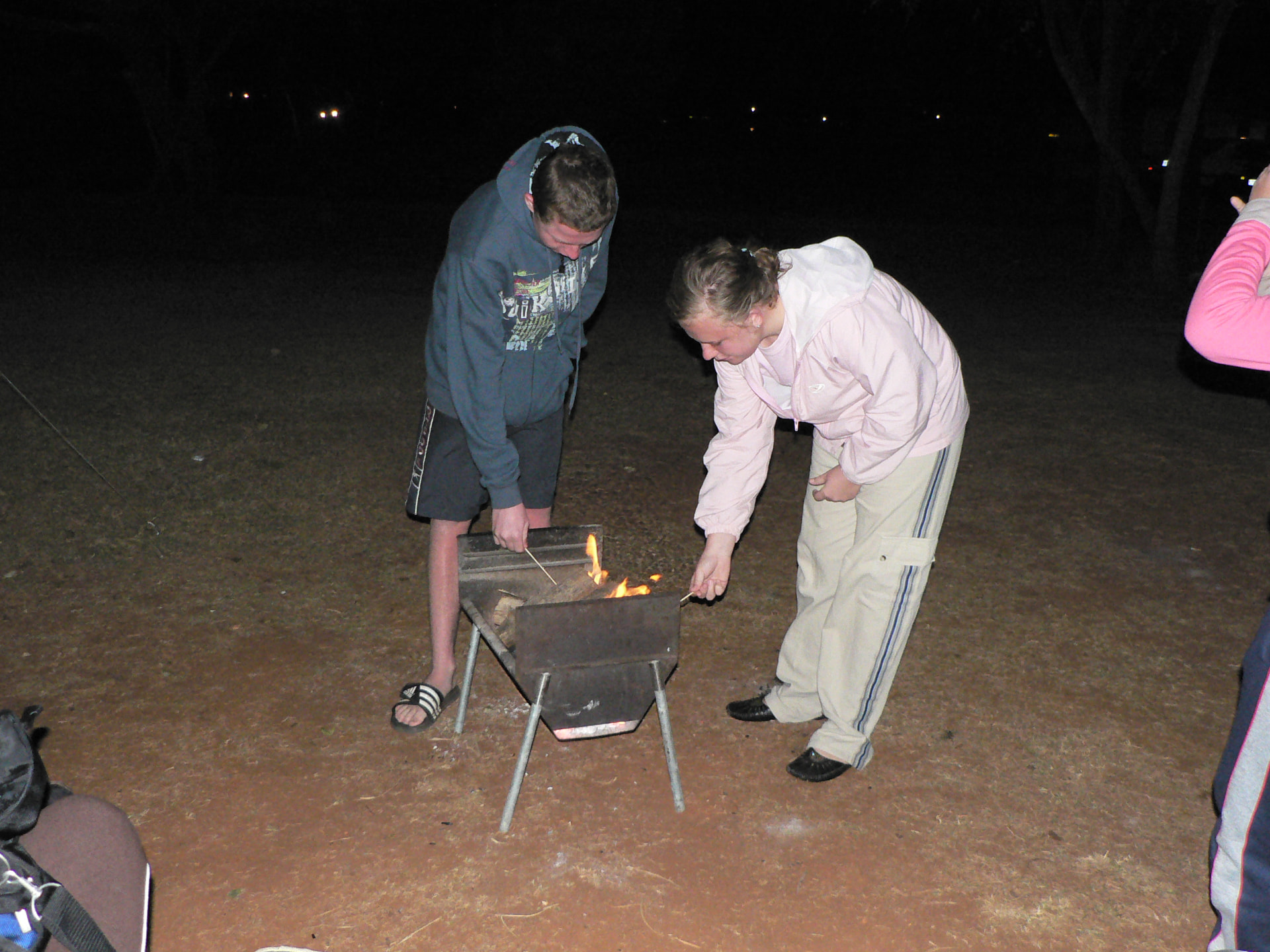 Angelo and a family member lighting a small fire together at night in the bush