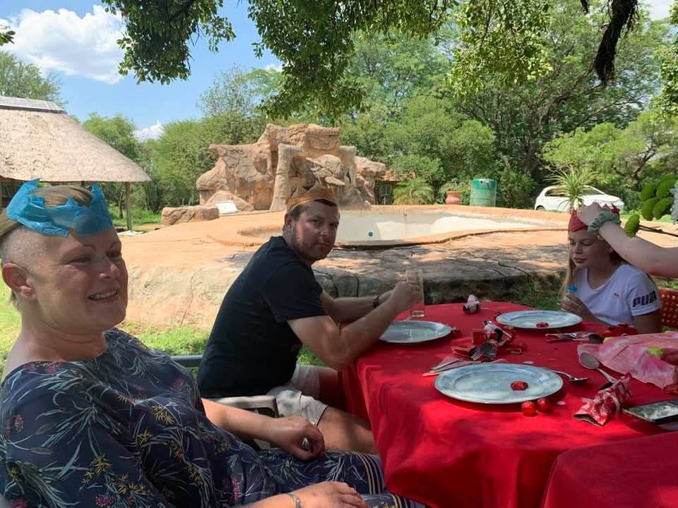 Angelo and family gathered at a red outdoor table wearing colourful paper crowns