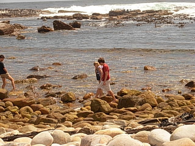 Angelo and family walking across the rocks at a rocky beach shoreline