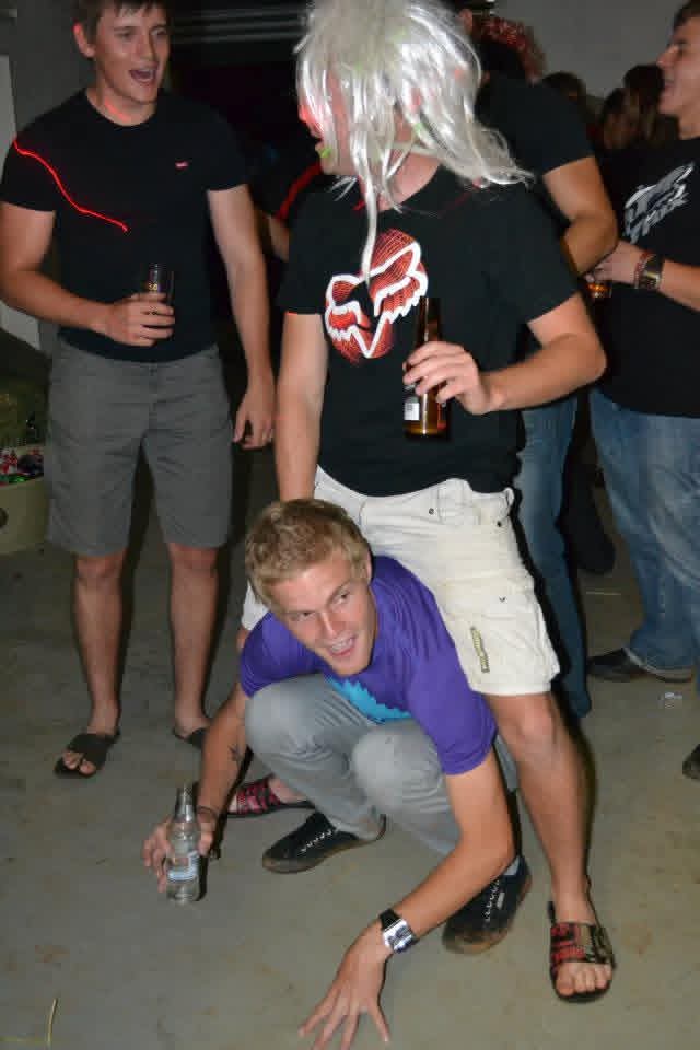 Angelo crouching playfully while a friend in a white wig stands over him at the party