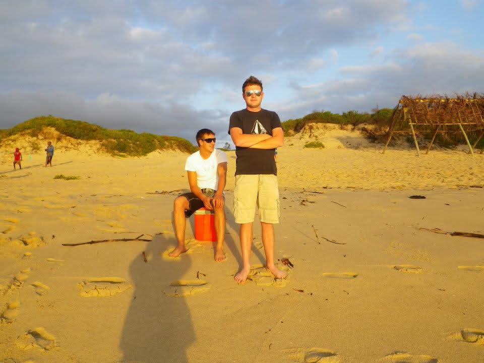 Two friends standing and sitting on the beach in the golden late-afternoon light