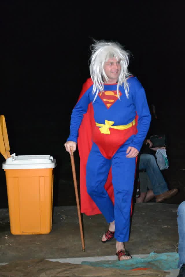 Angelo wearing a blue and red superhero costume and a white wig at an outdoor gathering at night