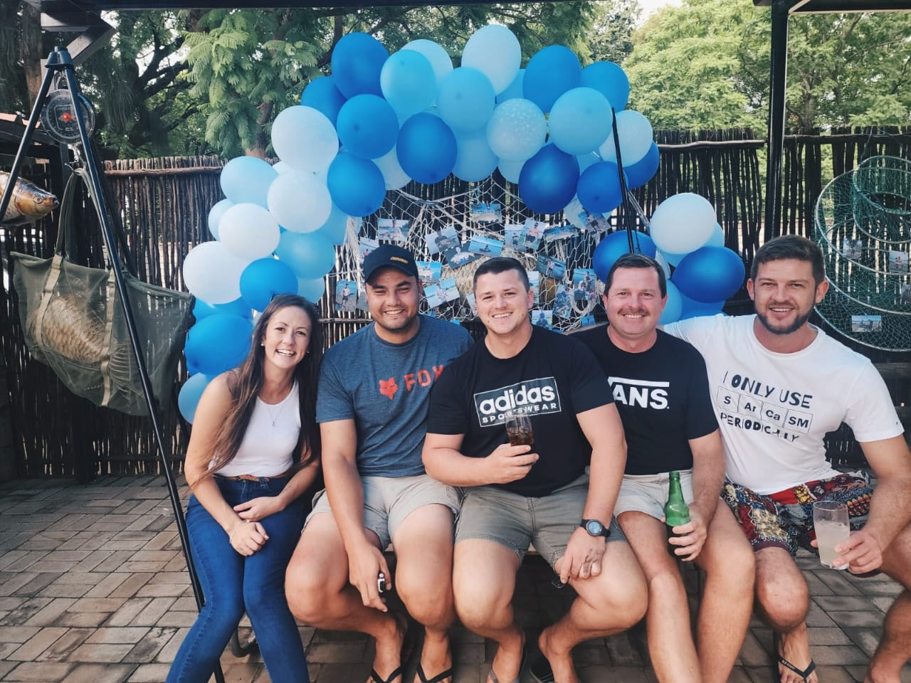 Five friends sitting together under the blue balloon arch