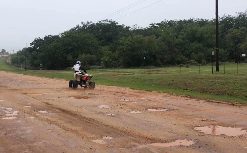 Angelo riding his quad bike along a wet dirt road beside the trees