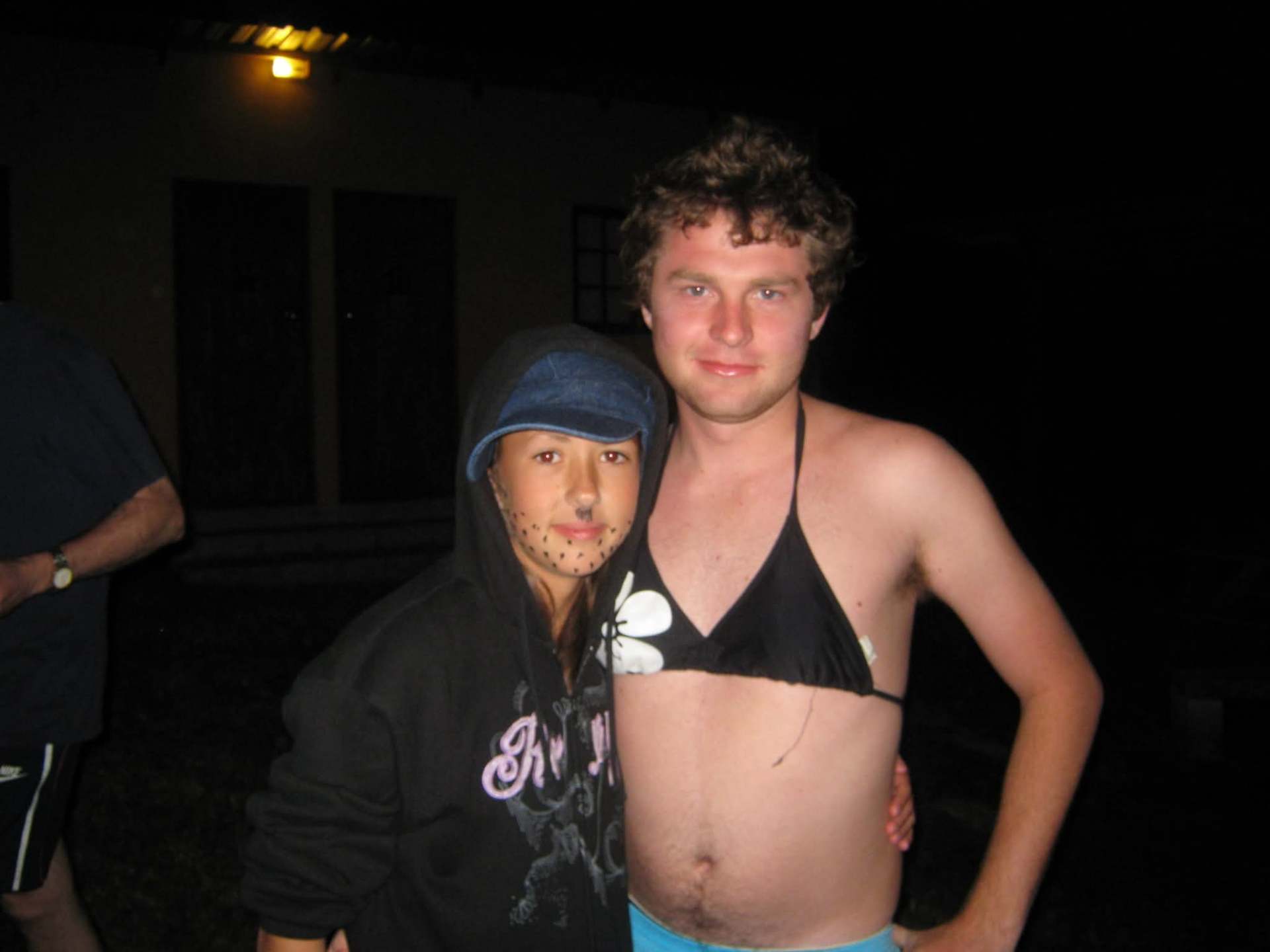 Angelo in a bikini top standing beside a friend in a hoodie at night