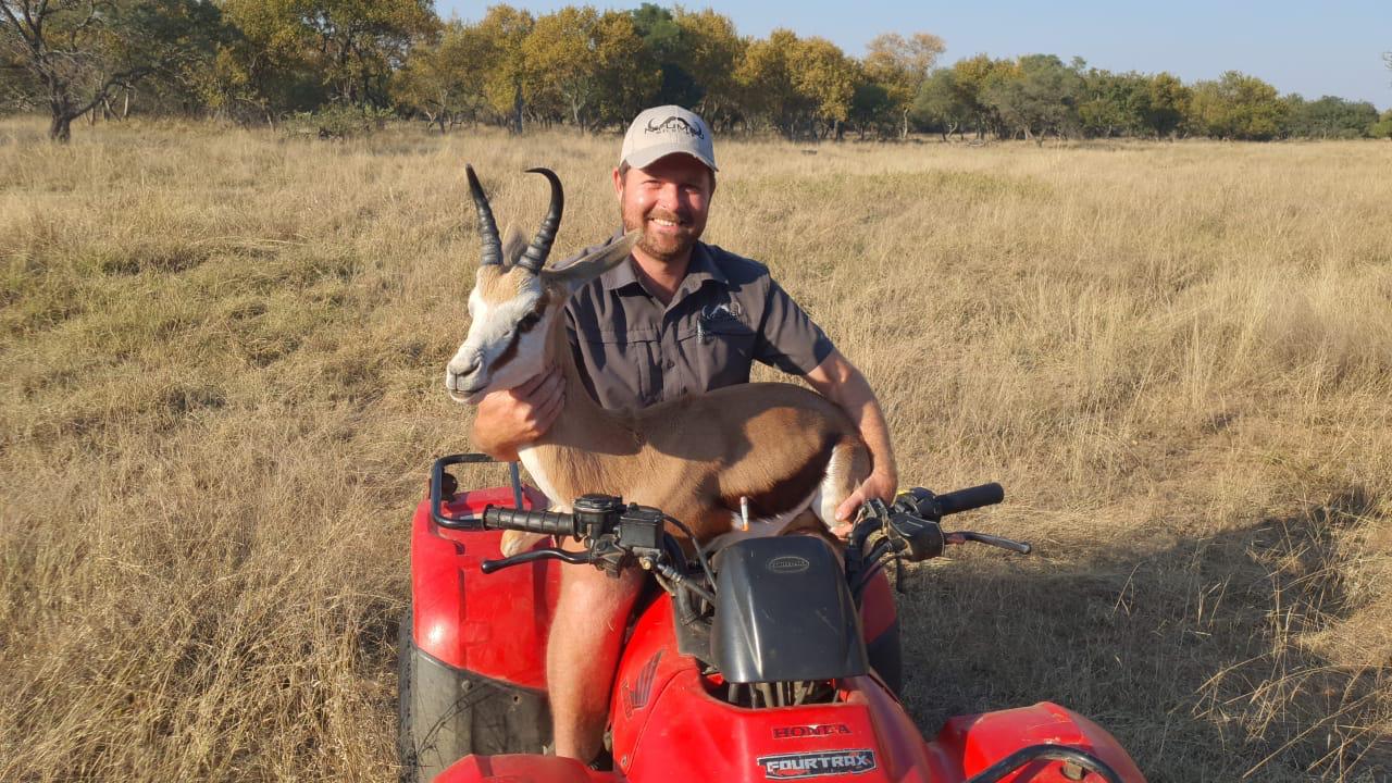 Angelo seated on a red quad bike holding a springbok ram across his lap